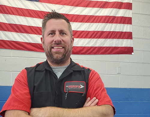 photo of Mike's Auto Service owner, Matt Bargren standing proudly in front of the American flag